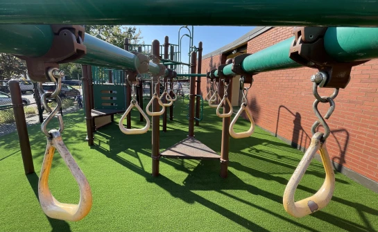 Safe playground surface with green synthetic turf and fall-rated padding under monkey bars at school in Pierce County