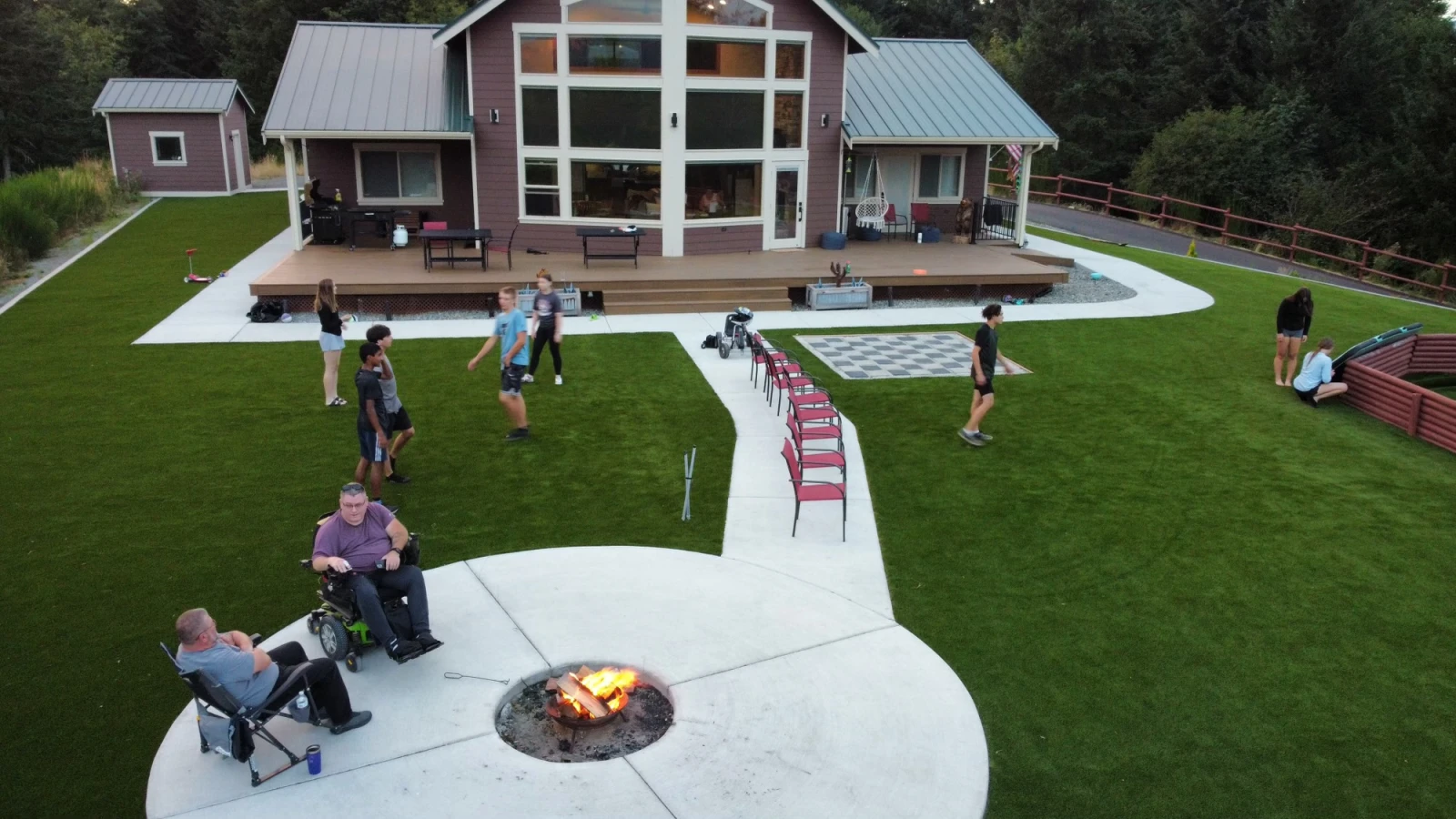 ADA compliant artificial turf installation with short pile height turf. Several kids playing on grass with adults hanging out by a fire.